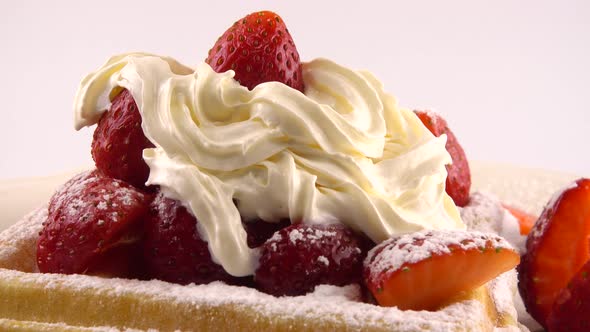 Belgian waffles with strawberry, whipped cream and powdered sugar on a plate on a white background.