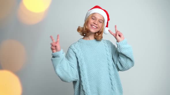 Happy Young Girl in Santa Claus Cap Show Peace By Fingers