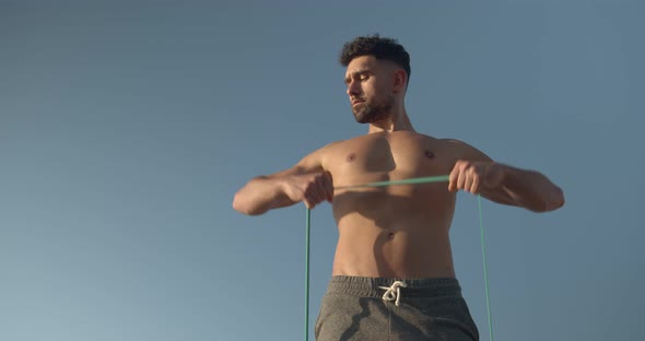 Determined athletic man training with elastic band near sea