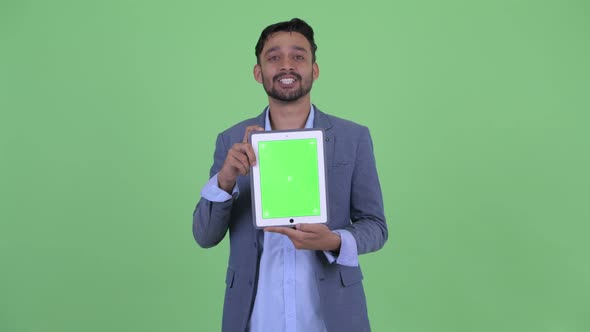 Happy Young Bearded Persian Businessman Talking While Showing Digital Tablet