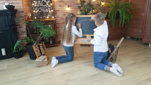 Blond schoolchildren - a boy and a girl draw a rainbow with multi-colored crayons