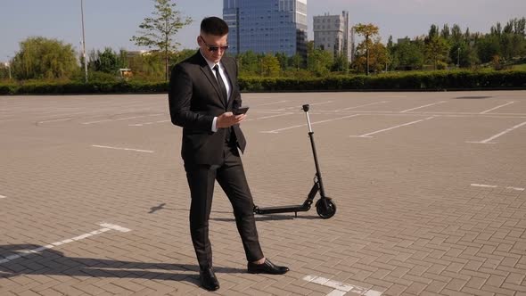 Closeup of a Businessman with a Phone and an Electric Scooter in a Park