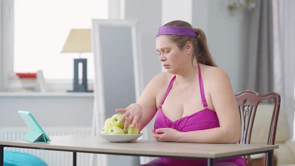 Sad Overweight Woman Eating Apple with Dissatisfied Facial Expression