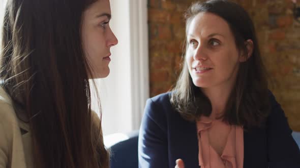 Portrait of two caucasian businesswomen sitting at table, talking, having business meeting