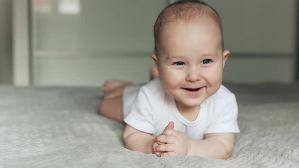 Cute Baby Lies on Bed Looking in the Camera and Smiling