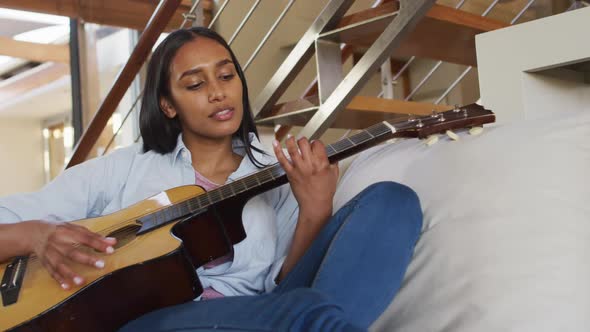 Mixed race woman on couch at home playing guitar and singing