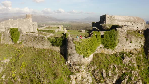 Drone flying backwards revealing travel couple standing on hill top old castle