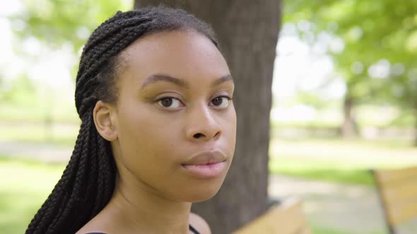 A Young Black Woman Takes Off a Face Mask and Looks at the Camera As She Sits on a Bench