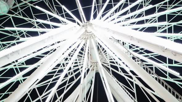 Bottom View of Ferris Wheel Spinning and Flashing White Lights at Night