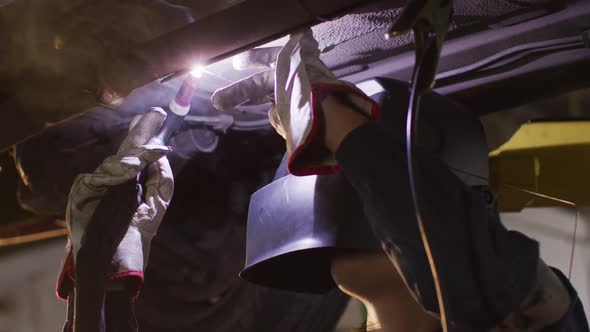 Female mechanic wearing welding helmet welding under a car at a car service station