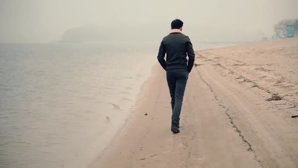 Man Walking On City Beach In Foggy Day. Guy In Sunglasses Walks On Sand. Man Walking On Sand Beach.