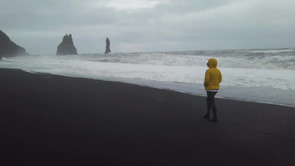 A woman walks on a black-sand beach in Iceland