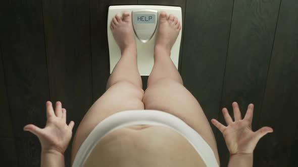 Overweight girl with fat belly standing on scales, word help on screen, angry