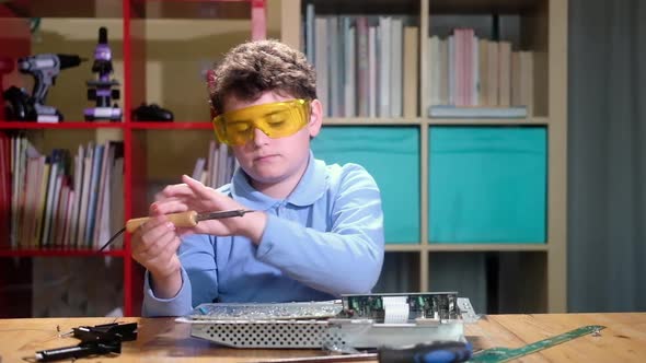 Child cute schoolboy at desk with tools is studying Electronics and repairing