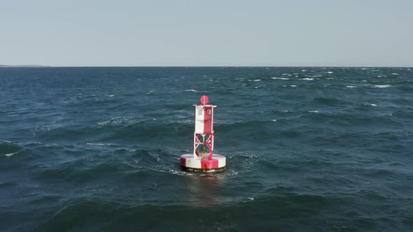 Aerial View of the Buoy Within the Bluish Sea Waves and Autumn Forest Behind