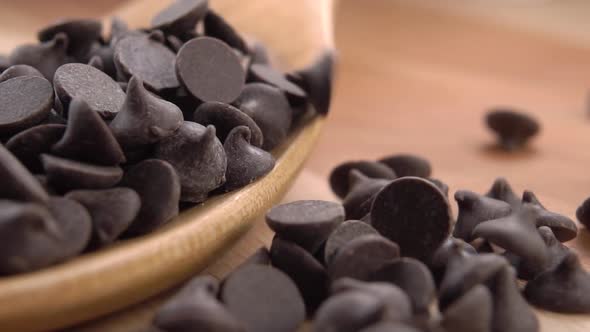 Dark chocolate chips falling into a wooden spoon. Slow motion. Macro