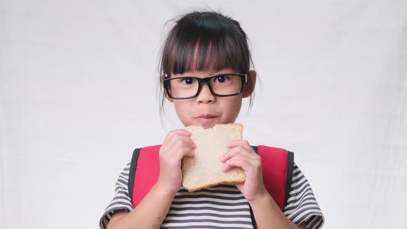 Cute schoolgirl having lunch at school. Cute little girl with bread on white background in studio. alt