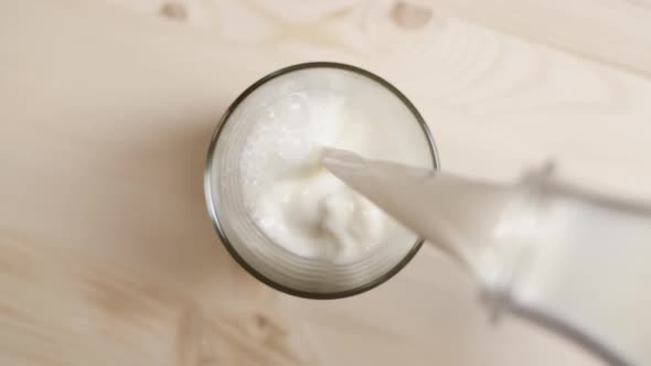 Top View of Milk Being Poured From Transparent Bottle in a Glass on Light Brown Wooden Table