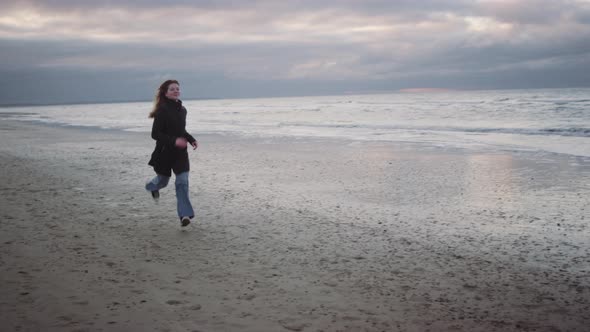 Redheaded Teenage Girl In Black Waving On Beach