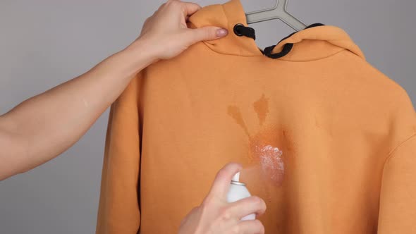 A Woman Uses a Stain Remover Spray on a Ocher Hoodie