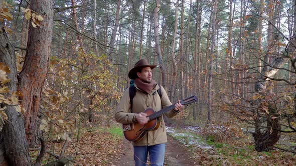 A Backpacker with a Guitar Walks Along a Trail in the Forest