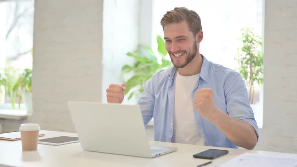 Successful Young Creative Man Celebrating on Laptop in Modern Office