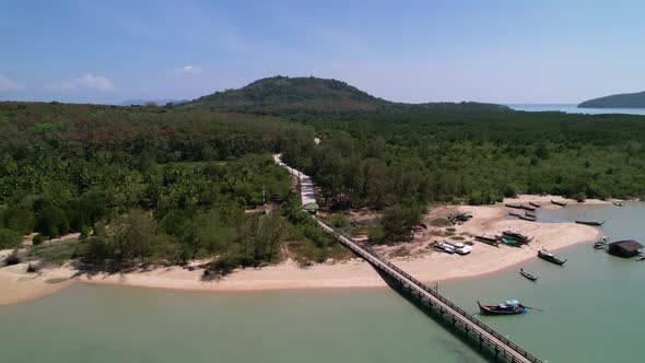 aerial circling a white sand beach on coconut island with a long pier in thailand
