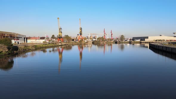 Low forward aerial of port cranes at port by still river, Buenos Aires