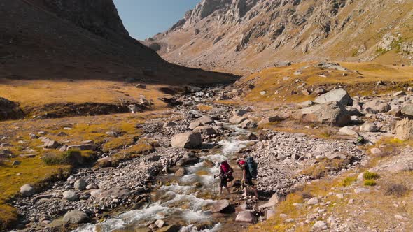 Hikers Crossing the River in the Mountains Aerial Shot