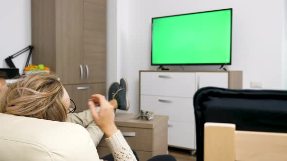 Happy Couple in Their Cozy Flat Watching a Big Screen TV with Green Screen on It