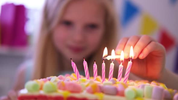 Blonde Caucasian Little Girl Lights Candles on Rainbow Cake Makes a Wish and Blows Them Out at