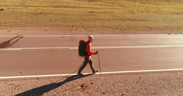 Flight Over Hitchhiker Tourist Walking on Asphalt Road. Huge Rural Valley at Summer Day. Backpack