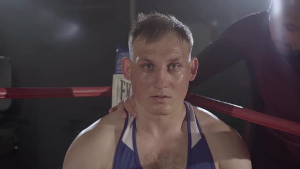 Trainer Endorsing Young Perspiring Boxer Sitting in Corner of Boxing Ring. Camera Approaches To