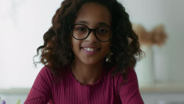 Smart Little African American Girl Wearing Eyeglasses Doing Hometask at Home Raising Head and
