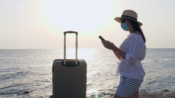 Woman in Protective Mask, Summer Clothes, Sunglasses, Sun Hat and with Travel Suitcase, Luggage