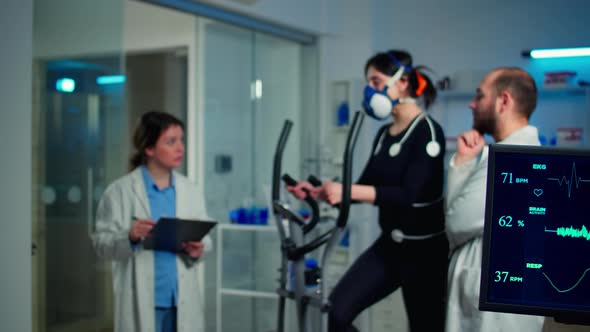 Sportswoman Running with Mask on Cross Trainer with Electrodes Attached To Body