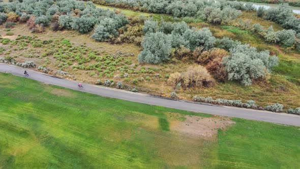 Mature couple riding bicycles along a nature trail by a calm river - aerial tracking view