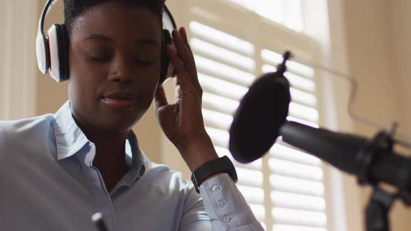 African american woman wearing headphones taking notes while looking at laptop