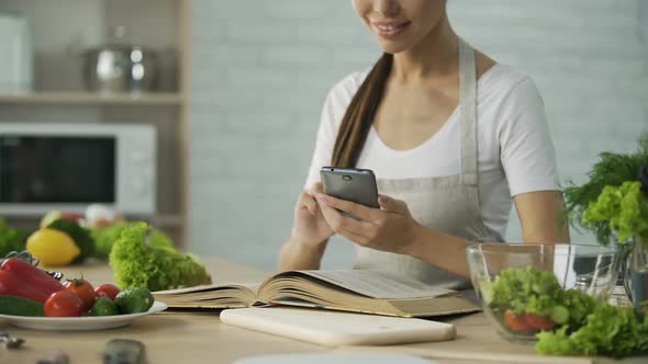 Pretty Woman Reading Cooking Book and Calculating Calories on Smartphone App