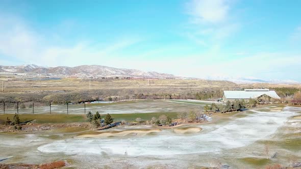 Aerial shot of a golf course with a light dusting of snow and mountains in the background - dolly ba