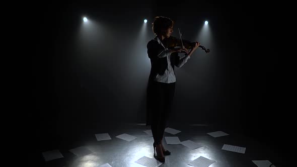 Dark Studio Girl Playing the Violin on the Floor Sheets of Notes. Silhouette. Black Smoke Background