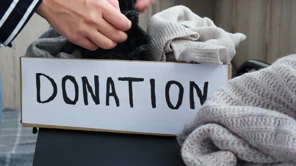 Female Volunteer Making Donation Box with Old Used Clothes Indoors