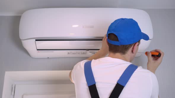 A young master in uniform repairs the air conditioner in the apartment.