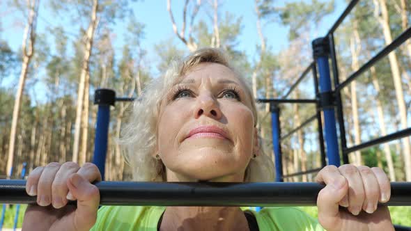 Mature Woman Does Pullups Smiling on Sports Ground Closeup