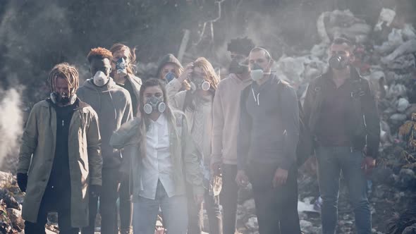 Group of Young People in Gas Masks Standing in the Toxic Smoke in a Garbage Dump
