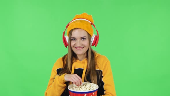 Portrait of Modern Girl in Big Red Headphones Is Watching an Exciting Movie and Eating Popcorn