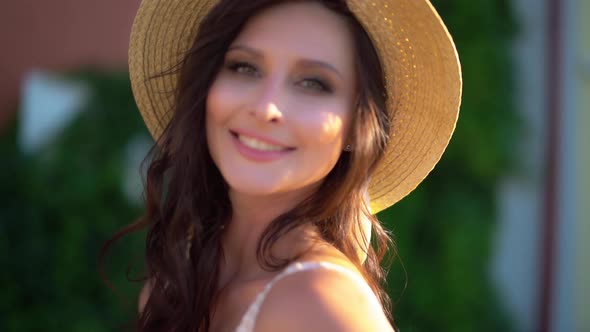 Cute European Brunette Girl with Flowing Hair in a Stylish Summer Dress and a Straw Hat