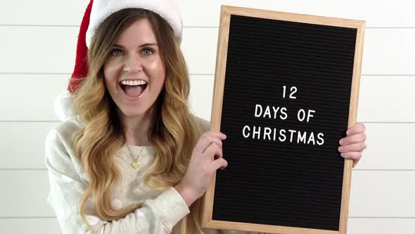 Woman smiles as she holds up sign saying, 12 Days of Christmas