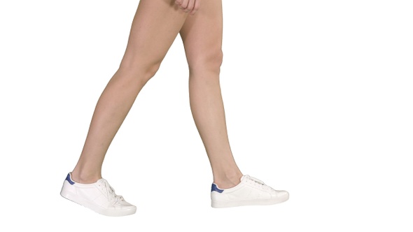 Women feet wearing white sneaker shoes walking on white background.