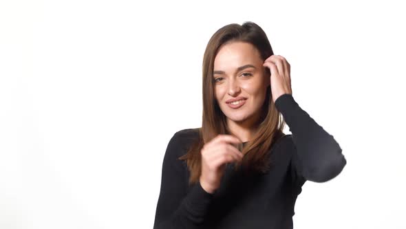 A sexy girl in black golf is posing and tidying one's her hair on a white background in the studio.